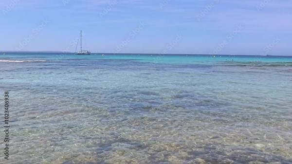 Static footage of Ibiza coastline captures the shimmering Mediterranean Sea with a distant catamaran The tranquil beach scene highlights clear blue waters and gentle sunlight reflecting on the surface