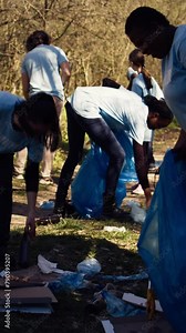 Group of diverse volunteers collecting rubbish from the woods and recycling in a garbage disposal bag, litter cleanup responsibility. Ecology activists picking up trash and plastic waste. Camera B.