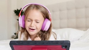 Emotional excited surprise child in headphones listening music and dancing on tablet computer on bed at home. Applications for children. Toddler listen to music