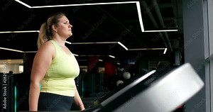 Young Plus Size Model, woman walking on a treadmill in gym near panoramic window, aerobic exercise and fat burning.