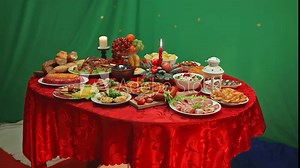Candlelit table full of food and food on green background. Bread, salads, fruits, vegetables, meat dishes. Bright Red tablecloth.