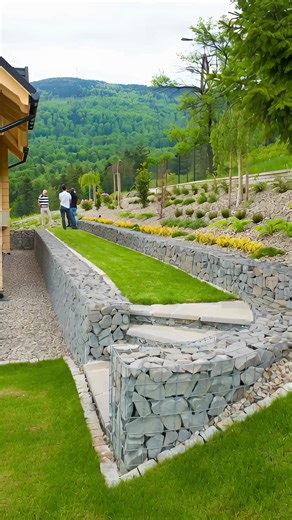 Modern Terraced Landscaping with Gabion Retaining Walls: A Smart Solution for Sloped Yards Sloped properties offer breathtaking views and unique character, but they also present design challenges. Uneven terrain can limit usable space, complicate drainage, and increase erosion risks. The landscape shown above demonstrates a modern and highly effective solution: tiered landscaping reinforced with gabion retaining walls. This approach transforms a steep yard into a functional, visually striking ou