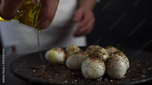 Cook kitchen Italian restaurant white robe, apron holds glass bottle yellow olive oil hand pours stream small mozzarella herbs spices black plate. Dairy product snack wine. Production advertis cheese Stock Video