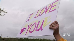 Because of the coronavirus, John Plocher can’t visit his wife, Leisa, in the hospital as she undergoes treatment for leukemia. Instead he’s been holding signs of love and support that she can see from her window. | NBC Nightly News with Tom Llamas