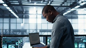 Engineer in data center operating notebook, deploying new server architectures. Server farm employee verifying settings using laptop, maintaining stable network performance, camera B