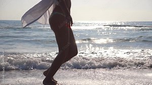 Feet of woman in bikini and shirt running on the sea waves at sunrise. Young beautiful girl jogging and having fun at sea shore. Summer vacation or holiday. Close up Side view Slow motion
