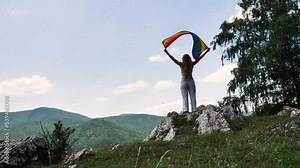 LGBTQIA month pride, rainbow peace flag against blue sky with clouds on a sunny day in mountains. Hold woman in hand and Celebrate Bisexuality Day or National Coming Out Day Stock Video