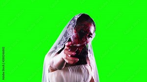 Scary zombie bride with bloody hand and wounded face threatening at the camera in the studio. Shot in 4k resolution with green screen background