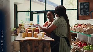 African american vendor giving food sample to shopper, recommending homemade snacks with organic ingredients. Vegan client trying out grocery store products before buying. Handheld shot.