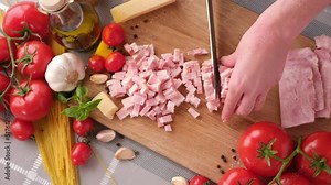 Making pasta carbonara - Slicing traditional pancetta bacon into pieces on a wooden cutting board with a knife