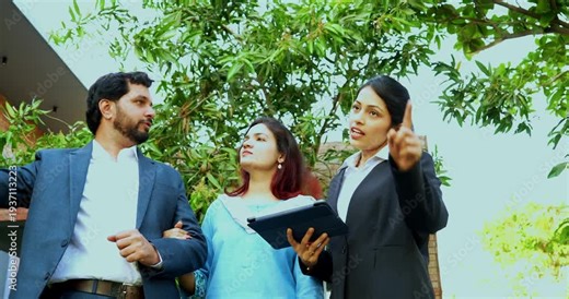 Indian woman event planner discussing with young couple outdoors in a lawn using a tablet computer to visualize the wedding or party layout during a successful professional consultation