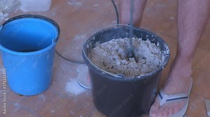 Builder is mixing cement plaster in bucket using an electric mixer, closeup view. Concept of construction and renovation works. Preparation of mortar for plaster and alignment of walls.