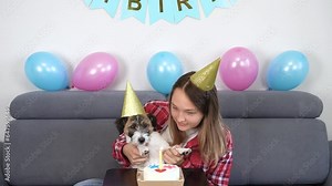 Girl with dog blowing out candles. Lifestyle. Portrait of a happy girl with her funny pet dog Jack Russell Terrier dog celebrating her birthday at home. Design by cake for a dog. Stock Video
