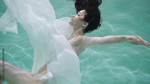 Underwater shot of a girl with black hair, a person slowly submerging underwater, with a caustic light effect