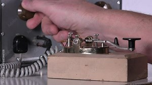 Morse code telegraph operator makes adjustments then types out message with telegraph key over radio station broadcast on vintage electronic hardware engineering military lab test equipment device
