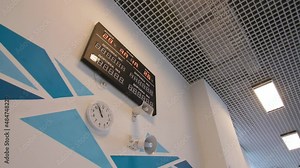 Digital scoreboard clock and loudspeakers on wall with blue pattern in hallway of contemporary sports stadium low angle shot