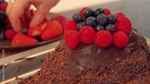 A woman puts blueberries and raspberries on the top of a chocolate cake - closeup on the cake
