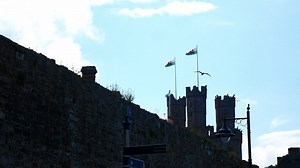 Caernarfon castle tower flag poles holding Wales welsh dragon emblems blowing in coastal breeze | Premium Stock Video Footage