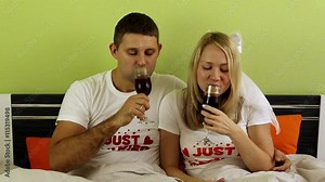 Couple drinking wine on the bed. Young couple drinking wine in the bedroom. Loving couple relaxing on the bed, romance. Just married, honeymooners, newlyweds. Honeymoon, young family.