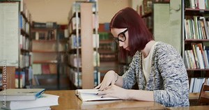 Pretty young girl is reading a book in the reading room of the library.