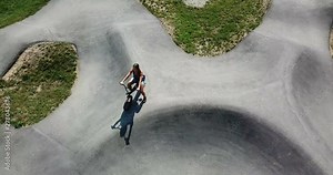 AERIAL 4K: Sport activity. Fit teenage girl sitting and smiling on a bmx bicycle on top of the concrete pump track skate park. Camera top down, circling subject.