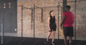 African American trainer grabbing ropes, guiding female client into rope waves on mat for strength