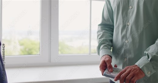 Bribe money cash exchange symbolizes corruption. A discreet payoff between men by a window, as a cash bundle moves hand to hand, implying kickback, extortion. Clear concept illicit cash bribe.
