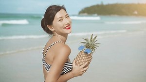 Belle jolie femme asiatique en bikini pinup s'amuse avec pinapple sur la plage tropicale paradise en regardant la caméra. Vacances en voyage, concept de régime fruité. Jeune fille qui profite de vacances d'été sur l'île tropicale
