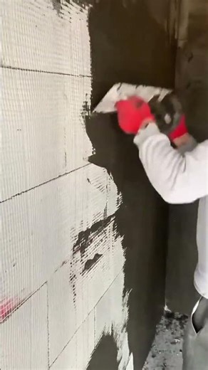 Applying a dark gray base coat of mortar over a reinforced mesh wall surface using