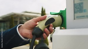 Hand pulling in cable from EV car charger or electric vehicle station. Cable connected at gas station, power supply battery charging an alternative eco environment future technology energy innovation.