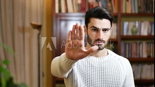 Handsome, serious young man doing stop sign with his hand with a severe expression.