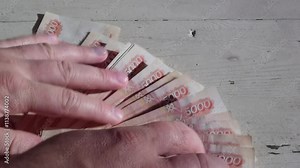Close up video. Man counts red paper russian cash money. Old white wooden table with cracks. Concept of loan, credit, debt, salary, currency exchange, pay, tax, bribe. 5000 rubles bills in male hand
