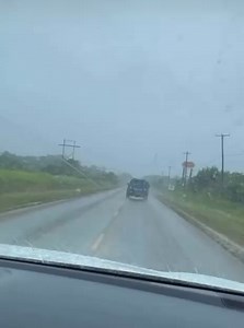 Rainfall drenches the scene as two individuals are escorted in the back of a mobile patrol unit. | Belize Live News