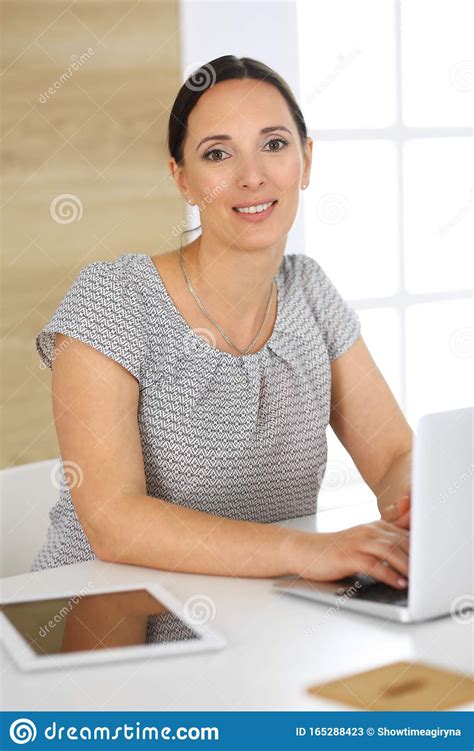 cheerful smiling business woman working with laptop computer while sitting at the desk in modern