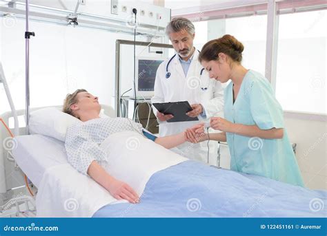 Doctor Examining Female Patient Lying On Bed In Hospital Stock Image