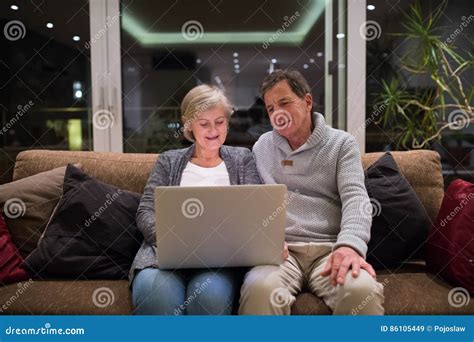 Senior Couple With Laptop Sitting On A Couch In Living Room Stock Image