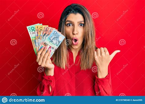 Beautiful Brunette Woman Holding Australian Dollars Surprised Pointing With Finger To The Side