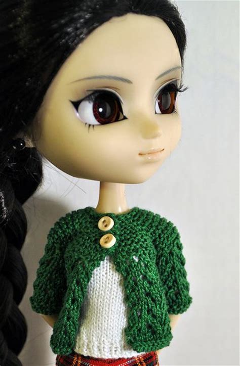 A Doll With Long Black Hair Wearing A Green Sweater And Red Plaid Skirt