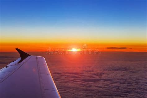 Airplane Wing In Flight Above The Clouds At The Sunset Background Stock