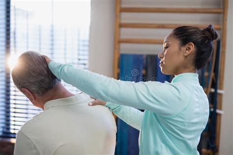 Female Therapist Examining Neck Of Senior Male Patient Stock Photo