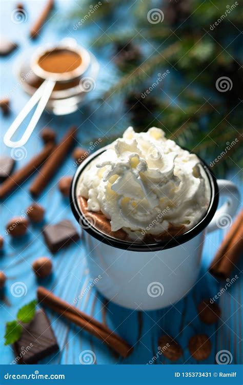 Mug With Hot Chocolate And Whipped Cream Among Cinnamon Sticks Nuts On A Blue Wooden Table