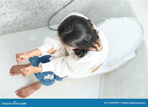A Woman Sits On The Toilet Bowl In The Bathroom And Take Off Her