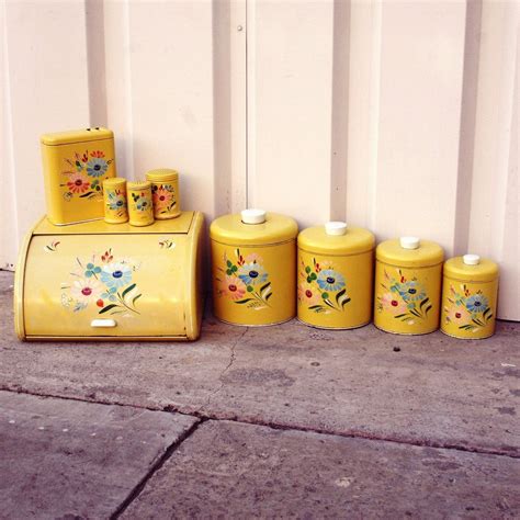 Four Yellow Canisters With Flowers Painted On Them Are Lined Up Against