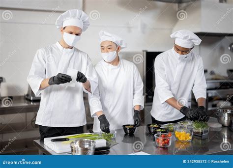 Chefs In Face Masks Prepare Takeaway Food In Professional Kitchen Stock
