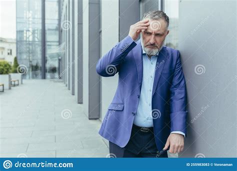 Senior Man Stands Near The Office Holds His Hand Behind His Head