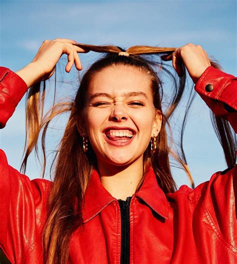 A Woman In A Red Leather Jacket Is Smiling And Holding Her Hair Up To