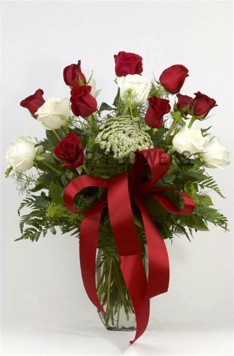 A Vase Filled With Roses And Greenery Wrapped In A Red Ribbon On A