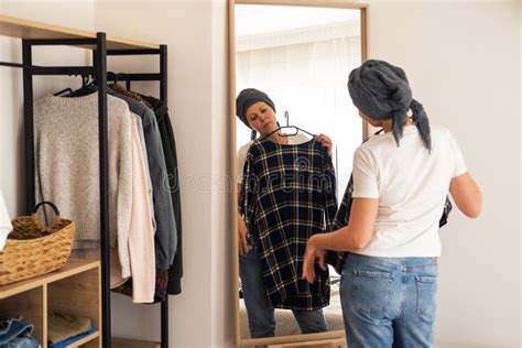 A Woman In A White T Shirt Tries On Clothes In Front Of A Mirror Stock