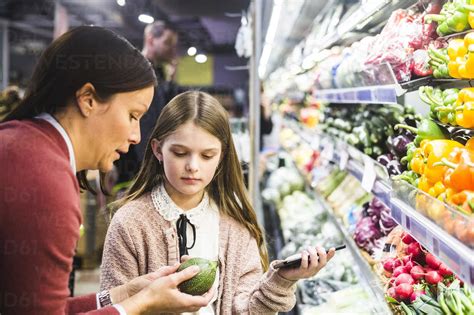 Mother Showing Cucumber To Daughter While Grocery Shopping In Supermarket Stock Photo