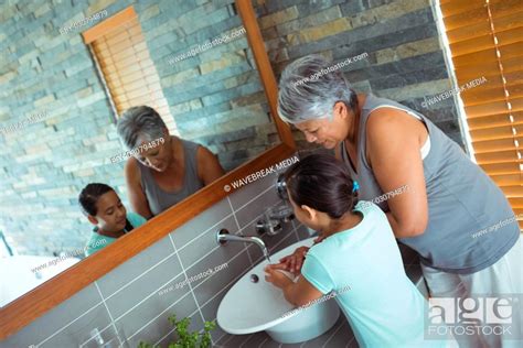 Grandmother And Granddaughter Washing Hands In Bathroom Sink Stock